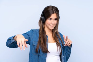 İzole edilmiş mavi arka planda müzik dinleyip dans eden Brezilyalı genç bir kız.