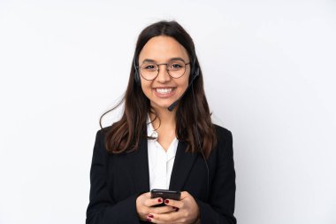 Genç pazarlamacı kadın beyaz arka planda izole edilmiş cep telefonuyla bir mesaj gönderiyor.