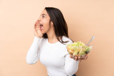 Genç esmer kız arka planda salata tutuyor ve ağzı sonuna kadar açık bağırıyor.