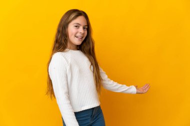 İzole edilmiş sarı arka plandaki çocuk, davet edilmek için ellerini yana uzatıyor.