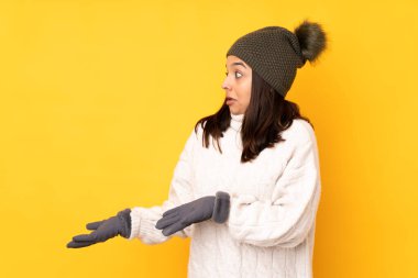 Kışlık şapkalı genç bir kadın izole edilmiş sarı bir arka plan ve şaşırtıcı bir yüz ifadesi var.