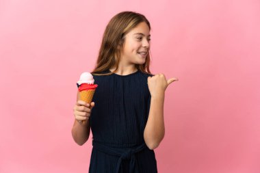 Kornet dondurması ile izole edilmiş pembe arka planı olan çocuk bir ürünü sunmak için kenarı işaret ediyor.