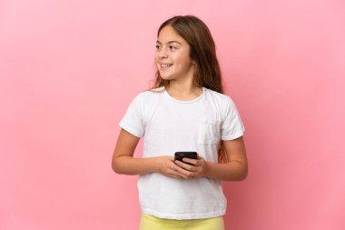 Pembe arka plan üzerinde izole edilmiş bir çocuk cep telefonu kullanıyor ve yukarı bakıyor