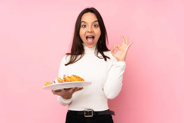 Jovem Morena Segurando Waffles Sobre Fundo Rosa Isolado Surpreso Mostrando — Fotografia de Stock