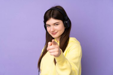 Genç Ukraynalı izole edilmiş mor arka plan kızı müzik dinliyor ve ön tarafı işaret ediyor.