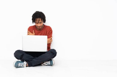 Genç Afrikalı Amerikalı adam yerde oturuyor ve laptopuyla donarak çalışıyor.