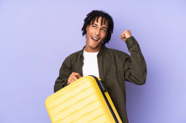 Genç Afro-Amerikan bir adam, mor arka planda izole edilmiş seyahat valiziyle tatilde.