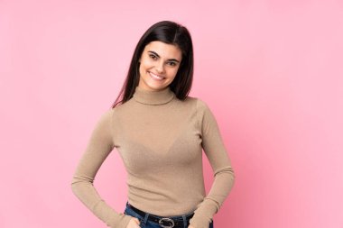 Genç bir kadın pembe arka planda gülüyor.