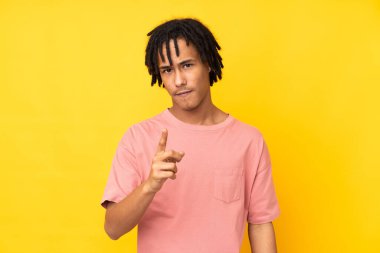Sarı arka planda izole edilmiş genç Afrikalı Amerikalı hayal kırıklığına uğramış ve ön tarafı işaret ediyor.
