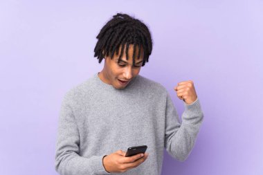Genç Afrikalı Amerikalı bir adam mor arka planda izole edilmiş. Şaşırmış ve bir mesaj gönderiyor.