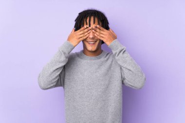 Genç Afro-Amerikalı bir adam mor arka planda izole edilmiş gözleri elleriyle kapatıyor.