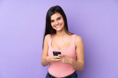 Mor arka plan izole edilmiş genç bir kadın cep telefonuyla mesaj gönderiyor.