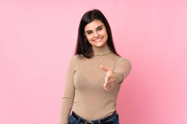 Soyutlanmış pembe arka planda genç bir kadın iyi bir anlaşma için el sıkışıyor.