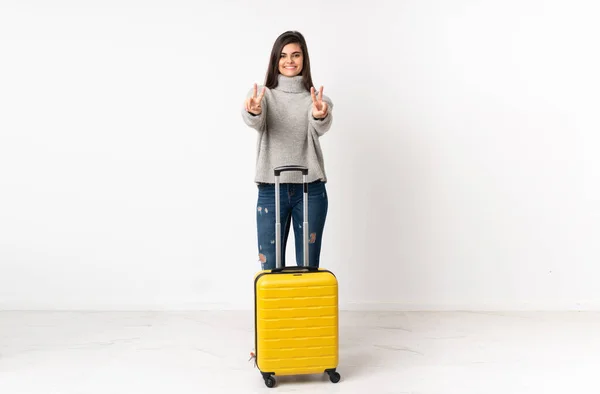 独立した白い壁の上にスーツケースを持つ旅行者の女性の完全な長さの体笑顔と勝利のサインを示す — ストック写真
