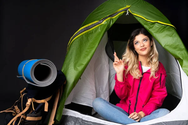 Teenager girl inside a camping green tent isolated on black background showing and lifting a finger in sign of the best