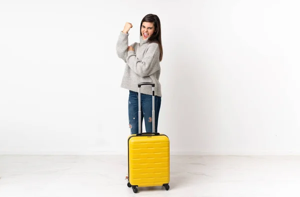 一个身材高大的女旅行家 提着一个手提箱从孤立的白墙上爬过去 做着强有力的手势 — 图库照片