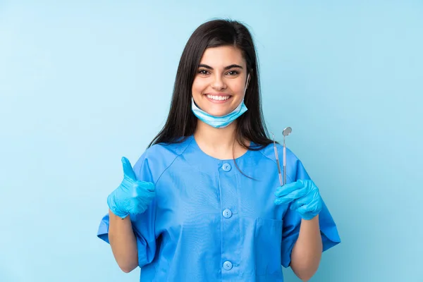 Młoda Kobieta Dentysta Trzyma Narzędzia Odizolowanym Niebieskim Tle Dając Kciuki — Zdjęcie stockowe