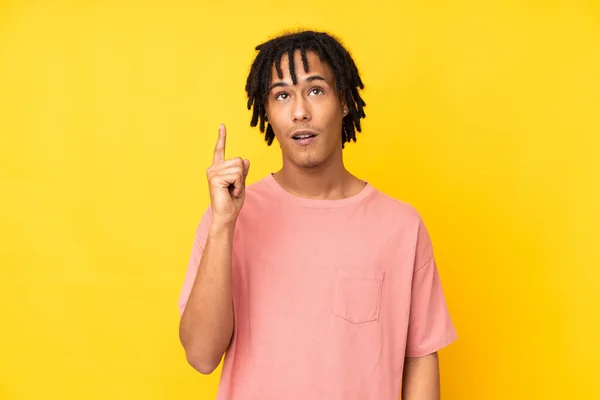 黄色の背景に孤立した若いアフリカ系アメリカ人の男は指を指差すアイデアを考えて — ストック写真