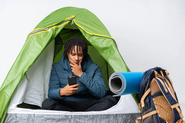 Young african american man inside a camping green tent thinking and sending a message