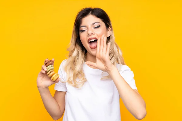 Menina Adolescente Isolada Fundo Amarelo Segurando Macarons Franceses Coloridos Gritando — Fotografia de Stock