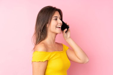 İzole edilmiş pembe arka planı olan Brezilyalı genç bir kız cep telefonuyla sohbet ediyor.