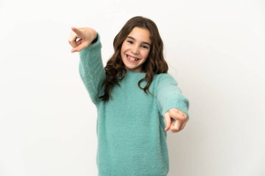 Beyaz arka planda izole edilmiş küçük beyaz kız mutlu bir ifadeyle ön tarafı işaret ediyor.