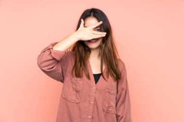 Pembe arka planda izole edilmiş beyaz bir kadın. Gözleri elleriyle kaplıyor ve gülümsüyor.