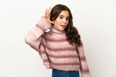 Beyaz arka planda izole edilmiş küçük beyaz kız elini kulağına koyarak bir şeyler dinliyor.