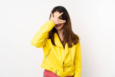 Beyaz arka planda soyutlanmış beyaz tenli genç bir kadın elleriyle gözlerini kapatıyor ve gülümsüyor.