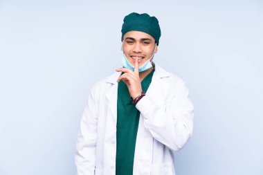 Mavi arka planda izole edilmiş üniformalı bir cerrah sessizlik hareketi yapıyor.