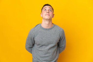 Genç beyaz adam sarı arka planda izole edilmiş ve yukarı bakıyor.