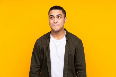 Asyalı yakışıklı adam sarı arka planda izole edilmiş gülümsüyor ve zafer işareti gösteriyor.