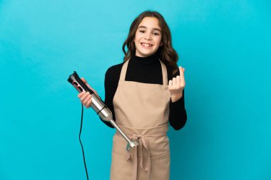 Mavi arka planda el blenderi kullanan küçük bir kız para hareketi yapıyor.