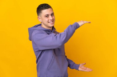 Sarı arka planda izole edilmiş beyaz bir genç ilan vermek için kopyalama alanı tutuyor.