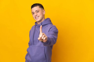 Sarı arka planda izole edilmiş genç beyaz adam parmağını kaldırıyor ve gösteriyor.