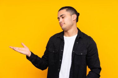 Asyalı yakışıklı adam sarı arka planda izole edilmiş. Durma hareketi yapıyor ve hayal kırıklığına uğruyor.