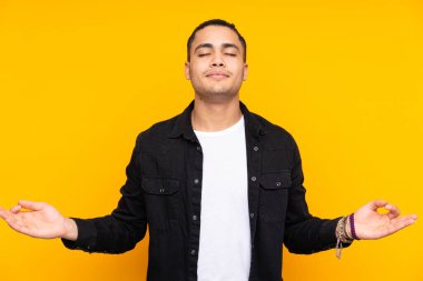 Asyalı yakışıklı, sarı arka planda izole edilmiş gergin ve korkmuş bir adam elleriyle suni teneffüs yapıyor.