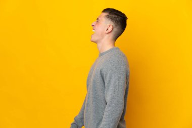 Sarı arka planda yalıtılmış genç beyaz adam yan yana gülüyor.