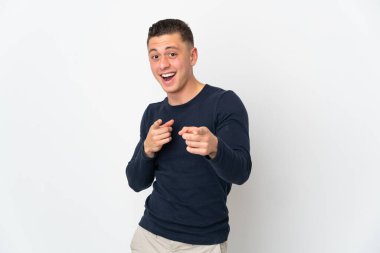 Beyaz arka planda izole edilmiş genç beyaz adam şaşırmış ve ön tarafı işaret ediyor.