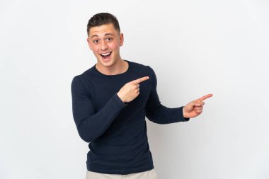 Beyaz arka planda izole edilmiş genç beyaz adam şaşırmış ve işaret ediyor.