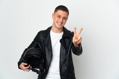 Beyaz arka planda izole edilmiş motosiklet kasklı beyaz adam gülümsüyor ve zafer işareti gösteriyor.
