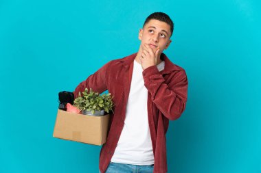 Kafkasyalı genç adam mavi arka planda izole edilmiş eşyalarla dolu bir kutuyu alırken harekete geçiyor.