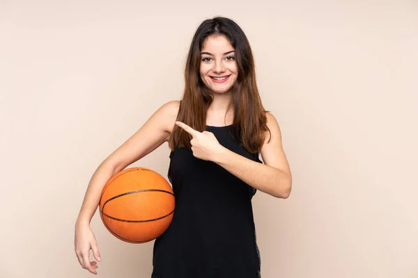 코카서스 여성은 베이지 배경에 고립되어 농구를 측면을 가리켰다 — 스톡 사진