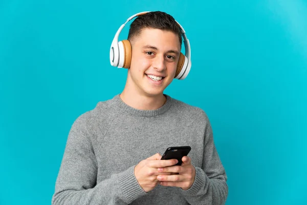 Νεαρός Καυκάσιος Άνδρας Απομονωμένος Μπλε Φόντο Ακούγοντας Μουσική Κινητό Και — Φωτογραφία Αρχείου