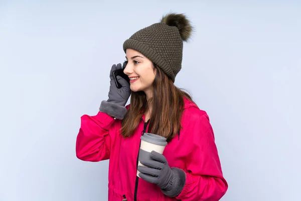 Giovane Ragazza Con Cappello Invernale Isolato Sfondo Blu Con Caffè — Foto Stock