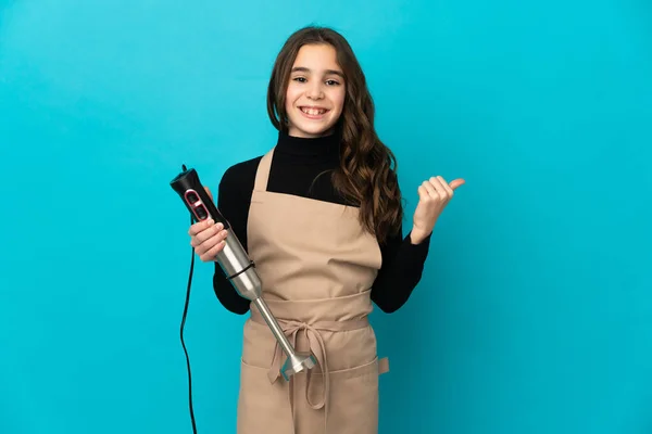 Menina Usando Liquidificador Mão Isolado Fundo Azul Apontando Para Lado — Fotografia de Stock