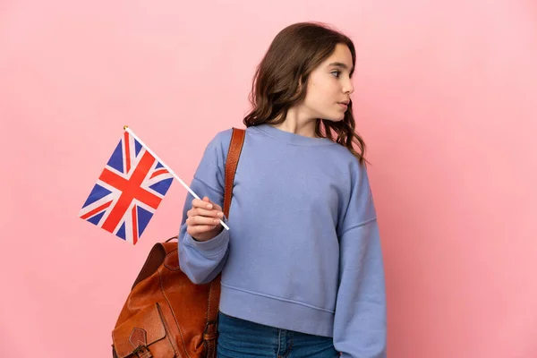 ピンクの背景で隔離された英国の旗を持っている女の子が側を見て — ストック写真