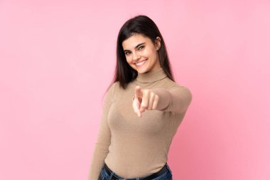 Soyutlanmış pembe arka plandaki genç kadın kendine güvenen bir ifadeyle seni işaret ediyor.