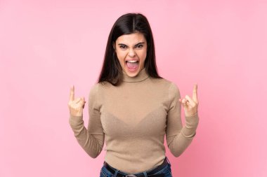 Soyutlanmış pembe arka planda genç bir kadın kaya jesti yapıyor