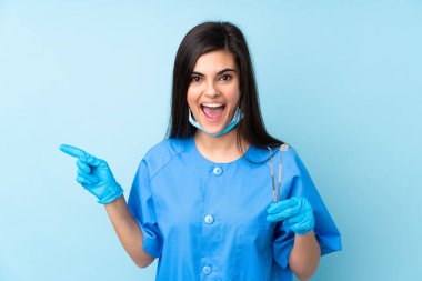 İzole edilmiş mavi arka planda aletleri tutan genç bir dişçi var.